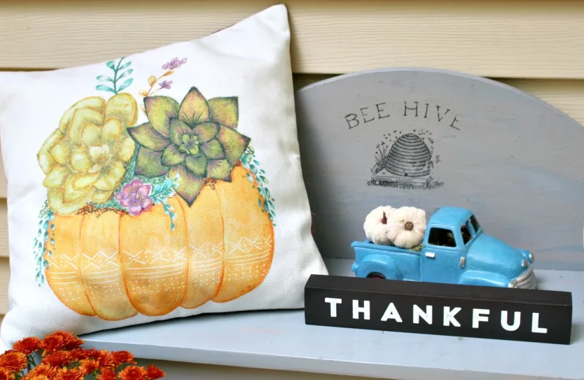 gray bench with pumpkin pillow and thankful sign