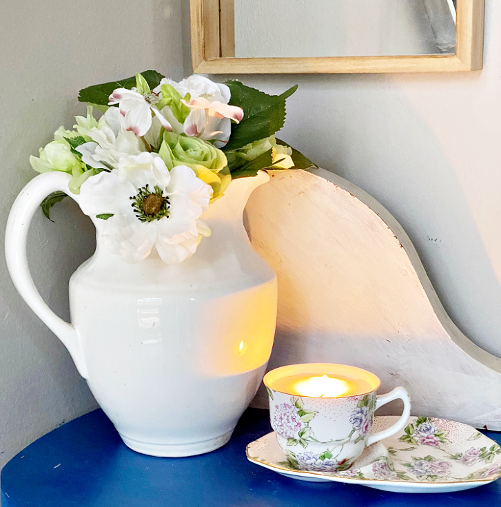 diy teacup candle on blue table with vase of flowers