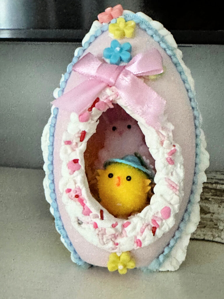 close up of a sugar Easter egg displayed on a mantel with pom pom chicks