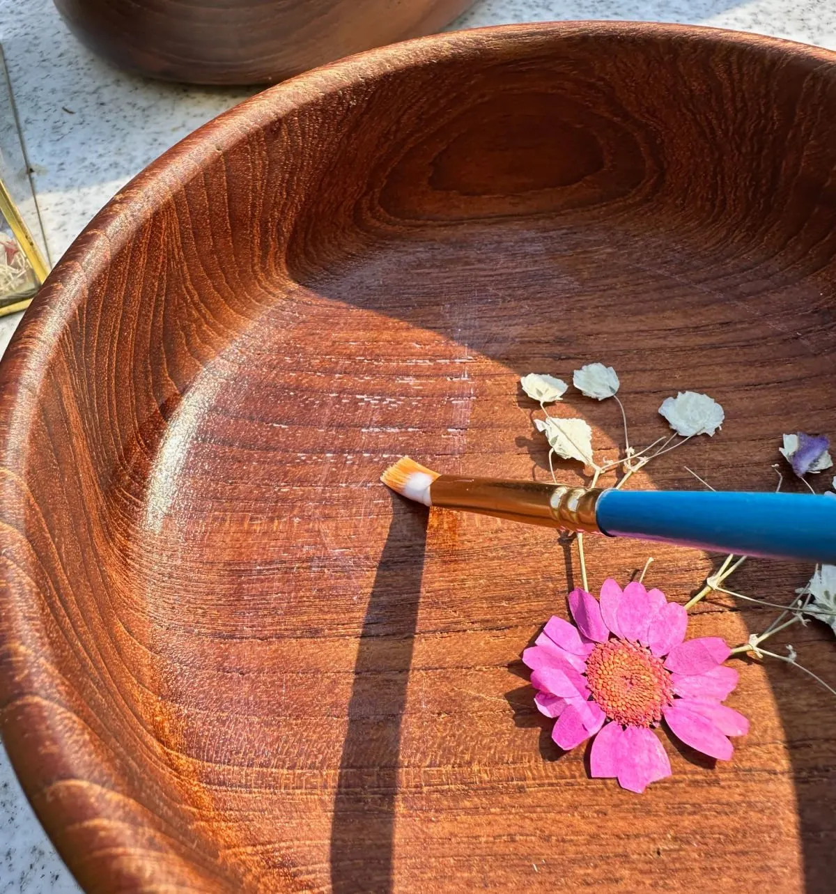 close up adding pressed flowers to wooden bowl with mod podge