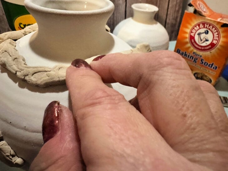 hand in picture shown adding clay trim to pottery barn inspired vase