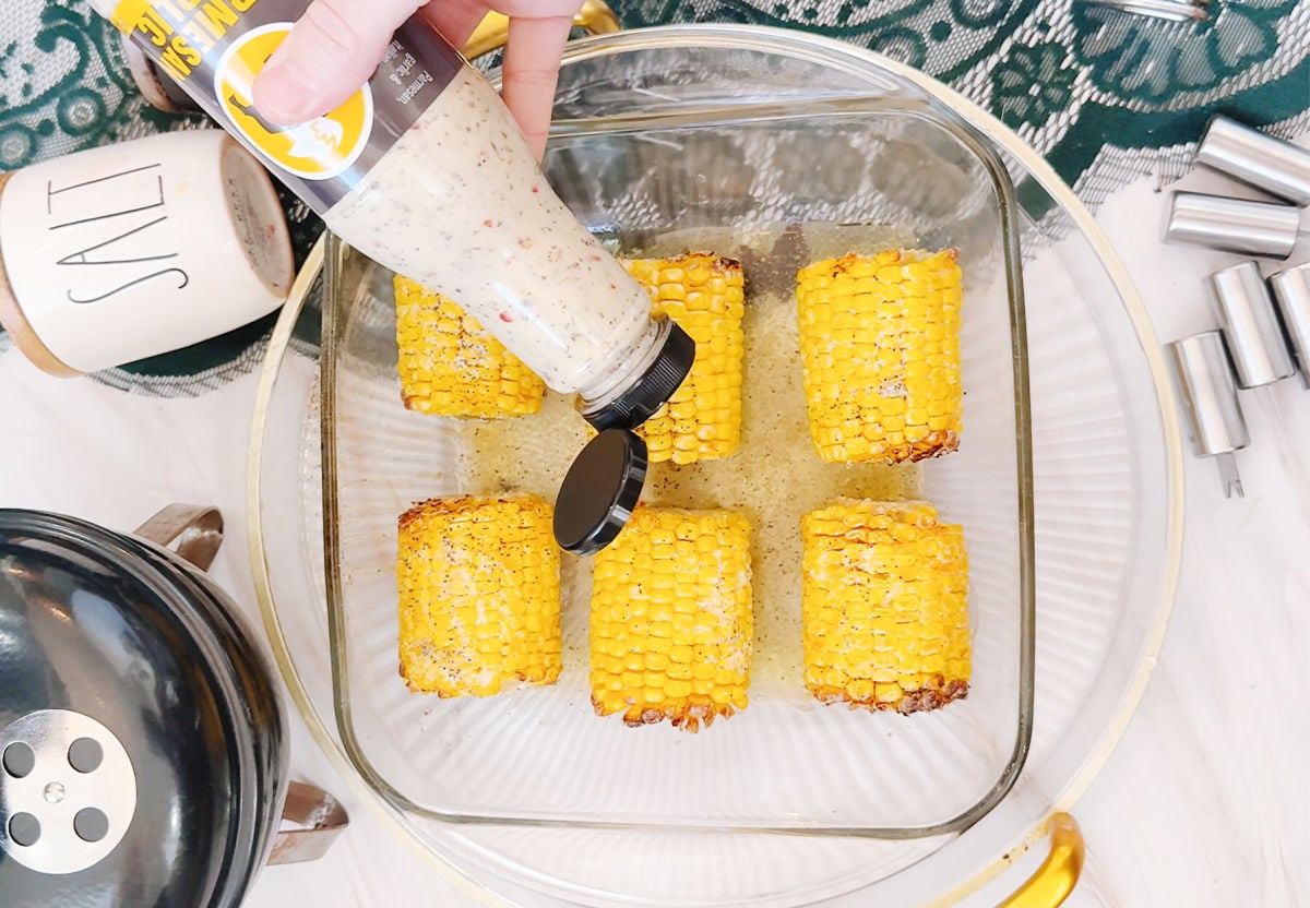 putting garlic parmesan on corn on the cobb
