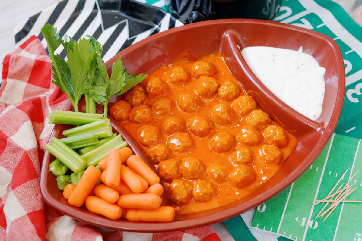 cooked crock pot meatballs with buffalo sauce in football tray served with carrots and celery